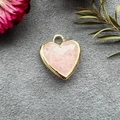 Detail of a pink crystal heart pendant with a gold frame on a grey velvet surface - Pink