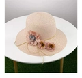 Close-up of pink straw sun hat with detailed fabric flower accents on a white table - Nude Pink