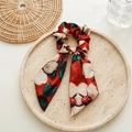 Nahaufnahme eines roten Vintage-Haargummis mit Blumenmuster und langen Bändern - Vintage Orangerot