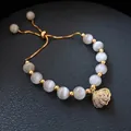 Detail of adjustable pearl bracelet with shell charm and gold beads on leather background - 10# Cat-Eye Shell Slider