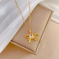 Macro detail of a gold bow pendant with square zircon on champagne brushed texture - Bowknot Necklace (D535)