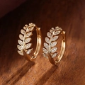 Detailed close-up of golden leaf earrings with micro-set zircons on textured wood - Gold