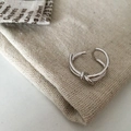 Primer plano de un anillo de nudo plateado sobre un fondo de bolsa de lino beige - Diseño de Nudo / Plateado