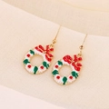 Detail view of Christmas wreath earrings with red bow and gold trim on white fabric - White Christmas Wreath
