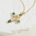 Dettaglio macro del ciondolo a croce in oro 14K con gemme verdi, perle e zirconi lucidi - Verde