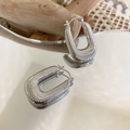 Detalle macro de pendientes en U de metal trenzado plateado con textura acanalada sobre espejo - Hebilla de oreja acanalada en forma de U / Plateado