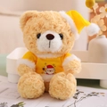 Close-up of a Christmas teddy bear wearing a yellow Santa hat and a Santa graphic T-shirt - Yellow T-shirt Style (Light Brown Bear)
