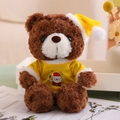 Close-up of a brown curly teddy bear wearing a yellow Christmas hat and a graphic T-shirt - Yellow T-shirt Style (Dark Brown Bear)