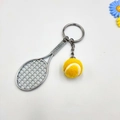 Close-up of a silver metal tennis racket keychain with a yellow mini felt ball on white background - Yellow