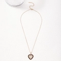 Golden heart pendant necklace with deep red zircon stones on white textured surface - Black Zirconia