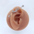 Makro-Detail des silbernen Industrial Barbell Ohrrings mit funkelnden Schmetterlingskristallen - Stil #6 Dreifach-Schmetterlingsreihe