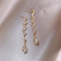 Dettaglio macro di lunghi orecchini a goccia dorati con zirconi su seta color champagne - Oro (Orecchini in Zirconia Lunga)