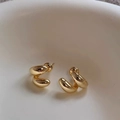Dettaglio ravvicinato di orecchini a spirale dorati su superficie in ceramica - Oro