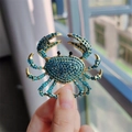 Detail shot of a golden crab brooch with blue rhinestones held by fingers - Blue