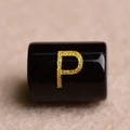 Macro shot of a black cylindrical bead with a golden letter P for DIY jewelry making - Letter P
