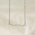 Macro shot of polished silver Mama letter pendant on a fine chain over beige fabric - Steel Color (KN282195-KLX)