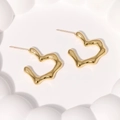 Detailed view of gold wave-patterned heart stud earrings on a white relief surface - Gold