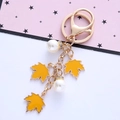 Detail shot of golden maple leaf keychain with elegant white pearls on a pink card - Single OPP Bag Packaging / Yellow
