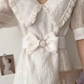 Dettaglio cintura elastica bianca con fibbia a fiocco in strass sopra un vestito - Bianco