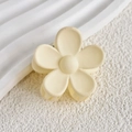Detailed top view of a matte yellow flower-shaped hair claw clip on a textured surface - Off White