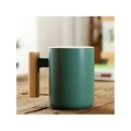Matte green ceramic mug featuring a cylindrical wooden handle on a wooden tabletop - Cylindrical Green Mug