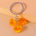 Primer plano de tres colgantes de corazón en resina ámbar con un llavero de metal plata - Naranja
