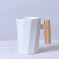 Minimalist white ceramic faceted mug with ergonomic wooden handle shown in a studio setting - Decagonal White Mug