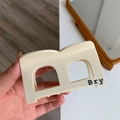 Primo piano di una molletta per capelli in acetato beige con scritta Bry nera in mano - Bianco Crema B Molletta