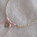 Détail du collier de perles avec un nœud rose et un pendentif cœur en argent - Style Croix Coeur Argent Antique