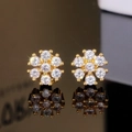 Vue détaillée de boucles d'oreilles fleurs dorées avec zircons étincelants sur fond noir - Doré