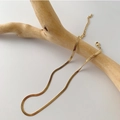 Detailed close-up of golden flat snake bone chain draped on a decorative wooden branch - Golden Titanium Steel Blade Chain