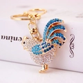 Llavero de gallo dorado con brillantes blancos y azules sobre una caja de regalo - Azul