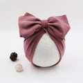 Detail of baby turban hat in dusty rose with large bow on white lace display stand - Purplish Red