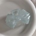 Close-up of a blue bow-shaped shark hair claw clip resting on a white ceramic plate - Translucent Blue Bowknot