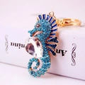 Sparkling blue rhinestone seahorse keychain with golden metal base on a white book - Blue
