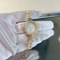 Detalle de reloj de cuarzo dorado con brazalete de hojas, cristales y esfera de nácar - Dorado