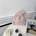 Close-up of pink and white geometric triangle knit wrist bag with minimalist accessories - Pink Triangle