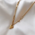 Detalle de un colgante de corazón dorado en una cadena de eslabones sobre seda blanca - Collar / Dorado