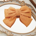 Elegant orange triple-layer bow hair clip made of textured fabric on a vintage mirror - Orange