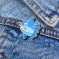 Macro shot of cute enamel ocean sunfish pin with gold metal edges on denim fabric - Blue Sunfish