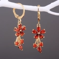 Makroaufnahme von Gold-Blumenohrringen mit roten Zirkon-Quasten am weißen Zweig - Rot