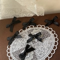 Detail view of six handmade black satin ribbon bow hair clips on elegant lace background - Black