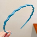 Blue wavy plastic headband for women being held against a minimalist grey background - Blue