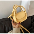 Close-up of pale yellow mini crossbody bag with leather texture and top handle detail - Yellow