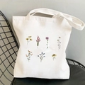 White canvas tote bag featuring yellow cosmos flower illustrations on a black chair - Mixed Botanical Flowers