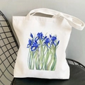 White canvas tote bag featuring a vibrant blue iris flower painting on a black chair - Blue Iris
