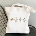 White canvas tote bag featuring vintage yellow cosmos flower prints on a metal mesh chair - Four-color Flowers Set