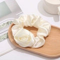 Detail eines weißen Satin-Haargummis mit Rosenblüte auf einem Vintage-Holztablett - Weiß