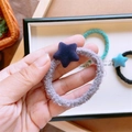 Détail d'un élastique en peluche gris avec étoile bleue dans un décor chaleureux - Étoile Violette