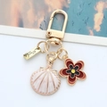 Detalle de llavero dorado con concha de esmalte blanco y colgante de flor roja - Concha Blanca